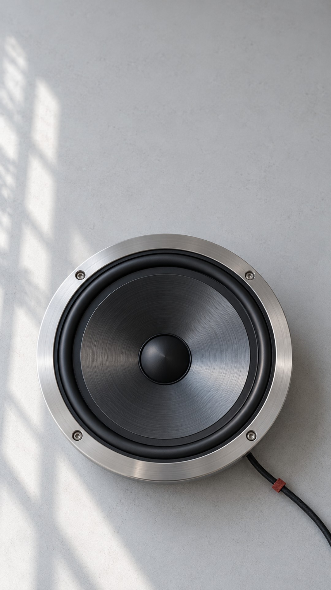 Brushed metal speaker on pale concrete, in natural daylight.